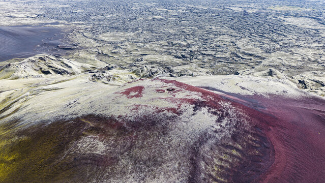 Aerial view of Laki volcanic crater featuring vibrant red volcanic soil and moss-covered terrain surrounded by vast, rugged lava fields in Skaftarhreppur, Iceland.