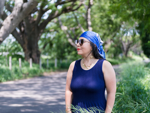Elegant Mature Woman in Blue Dress and Sunglasses in a Green Park