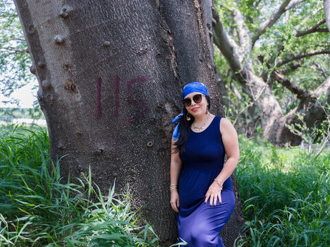 Woman in Blue Dress and Head Scarf Posing Beside a Large Tree