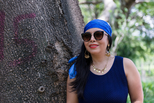 Woman in Blue Dress and Head Scarf Posing Beside a Large Tree