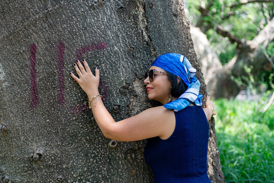 Woman in Blue Dress and Head Scarf Embracing a Large Tree