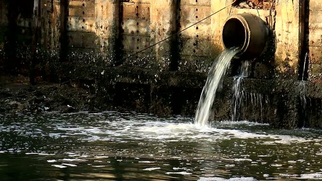 Wastewater Flowing From Drainage Pipe Into Polluted River Beside Concrete Wall