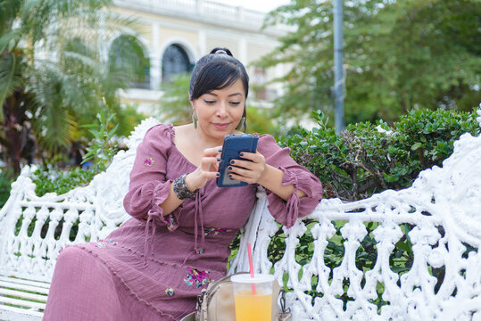 Latina Woman Typing on Smartphone While Sitting on White Bench Outdoors