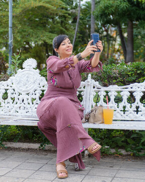 Cheerful Woman in Purple Dress Taking Selfie With Smartphone in Green Park