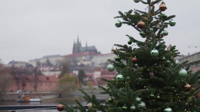 Christmas tree elevated view down a river passing beneath a sequence of stone and steel bridges, in Prague, red tiled roofs and green domes receding into winter haze, bare branches framing.