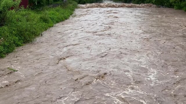 Overflowing Tarnava Mica River after heavy rain in Romania. Muddy, brown water flowing rapidly, creating a dangerous and destructive flood