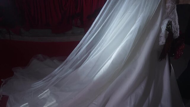 Bridal veil lifting over satin gown with lace trim against burgundy curtain, with wedding, bridal, veil, tulle detail, showing lace, satin, fabric, drape context
