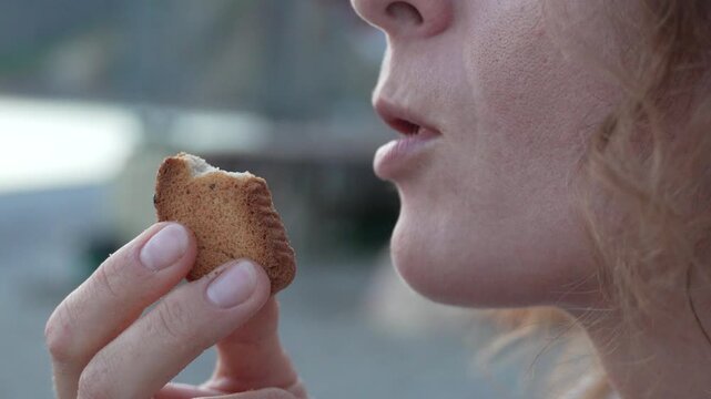 Mouth and hand of person tasting crunchy pastry outside. Macro close-up shot focusing on food texture.