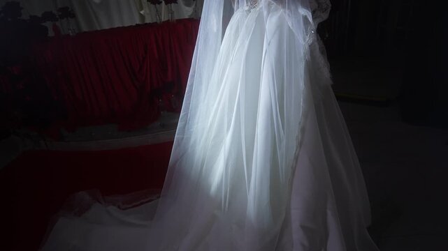 Illuminated bridal gown skirt and veil under soft directional spotlight in dim dressing area, with wedding, dress, veil, tulle detail, showing lace, fabric,skirt,gown context
