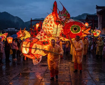 Traditional chinese lantern parade with giant glowing fish and animal lanterns on rainy festival street