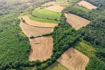Naklejka premium Aerial drone view of harvested fields with hay bales scattered across a rolling summer landscape.