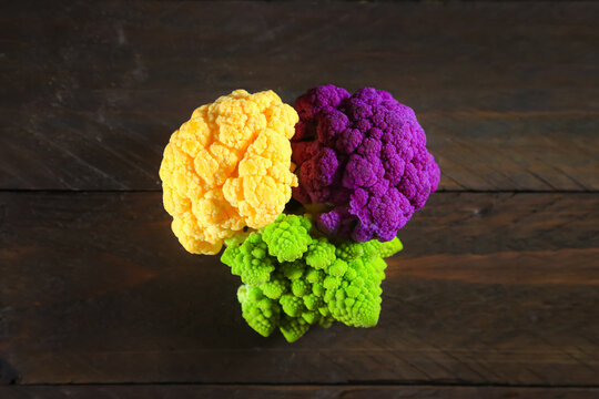 Multicolored cauliflower on a wooden table. Purple, yellow, and green florets.