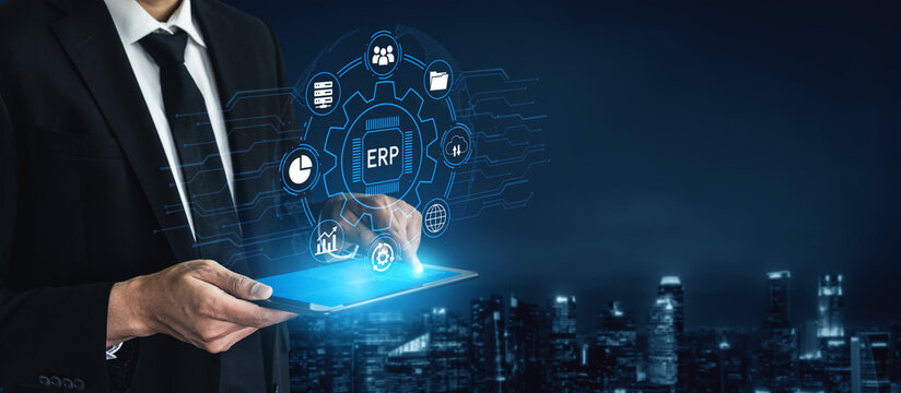 A businessman interacts with a tablet showcasing modern ERP software, illuminated by digital icons against an urban night skyline, symbolizing tech-driven business solutions. Entropy.