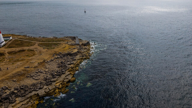 Aerial view of Portland Bill Lighthouse situated on the rocky coastline of the Isle of Portland with a small boat in the sea, Portland, Dorset, United Kingdom.
