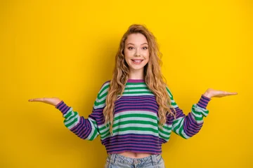 Fotobehang Onderzeeër Young woman in colorful striped sweater smiling with arms outstretched against bright yellow background  © deagreez