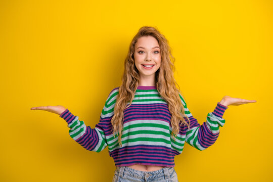 Young woman in colorful striped sweater smiling with arms outstretched against bright yellow background