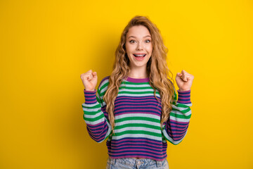 Naklejka na ściany i meble Bright young woman in striped sweater poses with excited smile against yellow background