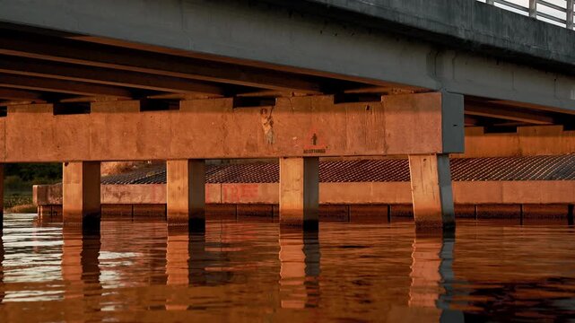 Detail shot of a concrete bridge's underside reflected in the still, sunlit waters of Lake Minneola in Clermont, Florida, at sunrise.