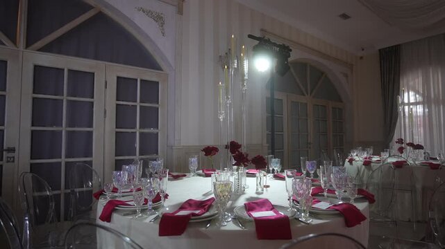 Elegant banquet table under spotlight in decorated reception hall with magenta napkins and rose centerpieces, with banquet, table, dinner, place detail, showing setting, glassware, napkin, plat