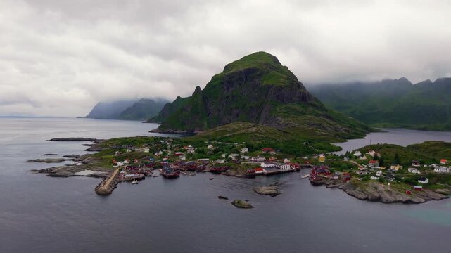 Aerial view of &Aring; fishing village at the southern tip of Moskenes&oslash;ya, with red rorbuer, rocky islets, sheltered harbor and dramatic mountains under cloudy skies in the Lofoten Islands, Norway