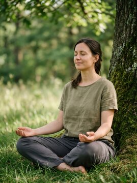 Woman meditating under tree in forest with eyes closed. Mindfulness and mental health concept with yoga breathing exercise for stress relief and inner peace
