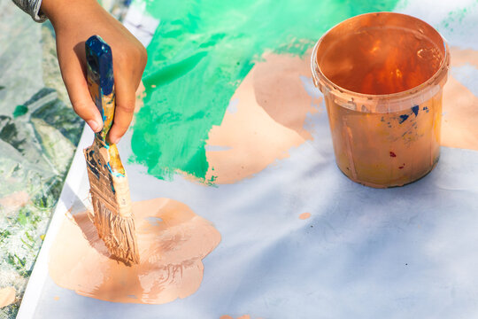 Child using a paintbrush to spread vibrant pink paint over a large white surface next to an open bucket of matching pink paint