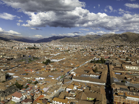 Aerial view of Old Town Cusco featuring dense terracotta-tiled rooftops, historic colonial architecture, and surrounding Andean mountains under a bright blue sky. Cusco, Cuzco, Peru.