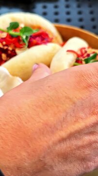Hand picking delicious bao bun with colorful vegetable salad from bamboo steamer.