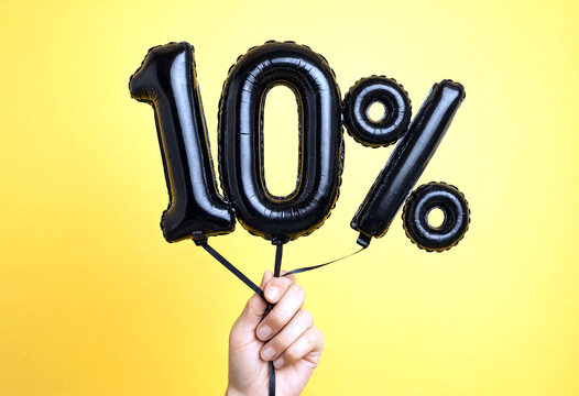 Hand holding black foil balloons shaped as ten percent sign on yellow background