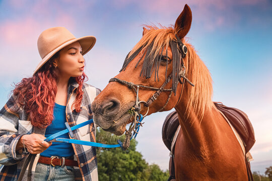 Young woman interacting with a horse in a natural setting at sunset, showing friendship