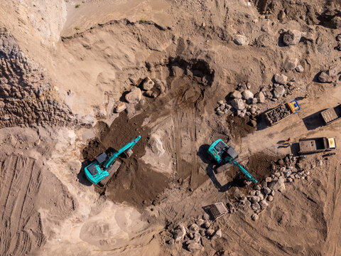 Aerial view of two excavators digging in a quarry with dump trucks parked nearby on a sunny day in Klaten, Central Java, Indonesia.