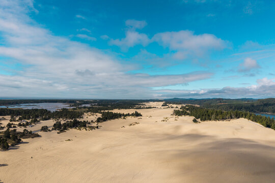 Aerial view of Coos Bay sand dunes featuring vast sandy landscapes, evergreen forests, and a blue sky with scattered clouds in Coos Bay, Oregon, United States.