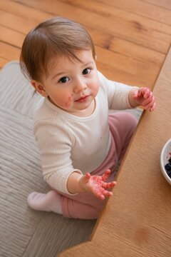 Toddler enjoying snack with messy hands sitting on wooden floor