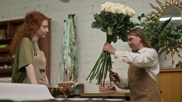 Low angle shot of two young adult Caucasian female florists working in flower warehouse, one trimming stems of large rose bouquet. Video is ideal for small business marketing