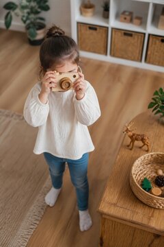 Young girl joyfully taking pictures with toy camera indoors