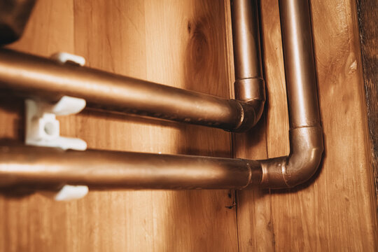 Close-up angled view of copper water pipes with elbow fittings mounted on a wooden wall panel. Plumbing concept.