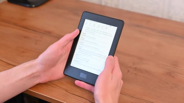 Modern digital reader device held above wooden table in casual setting