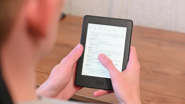 Student holds electronic reader for study session on wooden desk
