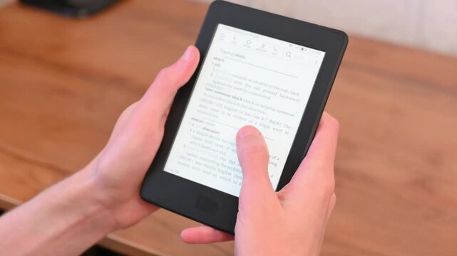 Student holds electronic reader for study session on wooden desk