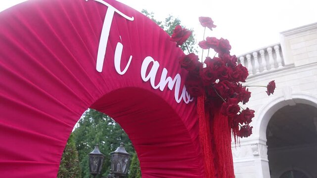 Low-angle magenta pleated arch with white cursive lettering and clustered red roses tilting outward, with arch, fabric, pleat, red detail, showing magenta,rose, bouquet, flower context