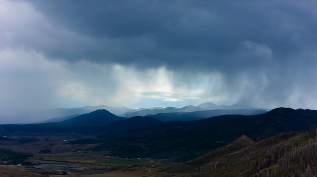 Aerial view of the mountainous landscape featuring dramatic storm clouds and rain showers over the rolling hills of Granby, Colorado, United States.