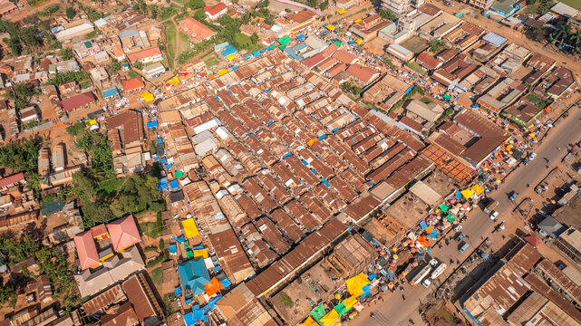 Aerial view of the bustling market in Mbale, featuring rows of stalls with metal roofs, colorful tarps, and surrounding urban infrastructure in Mbale, Eastern Region, Uganda.