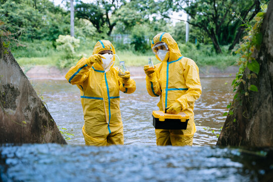 Environmental scientists in yellow protective suits analyze polluted water samples in glass flasks