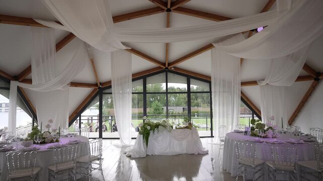 Interior wedding reception hall with vaulted wooden beams, sheer drapery, centered head table and daylight window view, with wedding, reception, banquet, venue detail