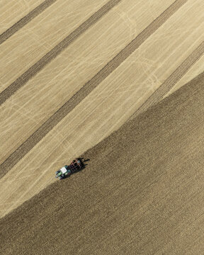 Aerial view of a tractor plowing a large agricultural field with distinct soil patterns in Aschheim, Bavaria, Germany.