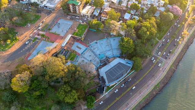 Aerial view of Manuel Antonio Ramirez Amphitheater surrounded by lush trees, urban streets, and the Parana River in Posadas, Misiones, Argentina.