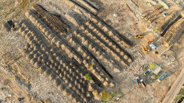 Aerial view of a waste management site with organized rows of waste, heavy machinery, and excavation equipment in India.