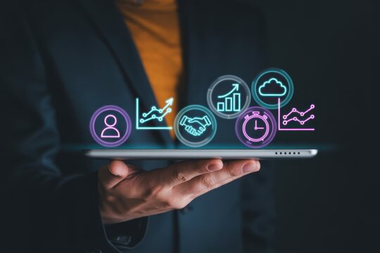 Business person holding a digital tablet with floating neon circular representing growth charts handshake cloud storage and time management for corporate strategy
