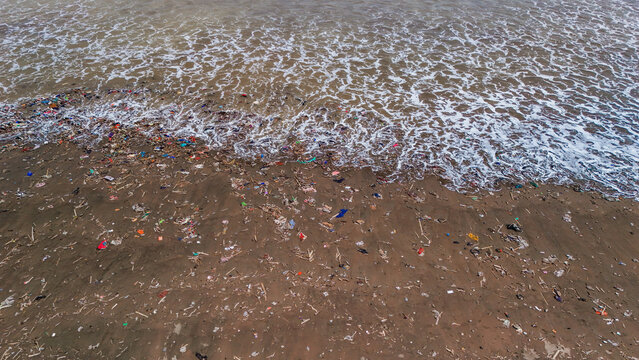 Aerial view of a beach heavily polluted with plastic waste and debris being washed up by ocean waves in Indonesia.