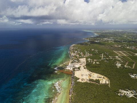 Aerial view of Beach Bay coastline with turquoise waters, sargassum seaweed, and lush tropical vegetation under a cloudy sky in Bodden Town, Bodden Town, Cayman Islands.